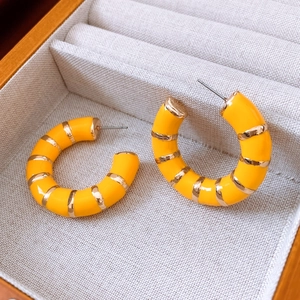 Macro shot of yellow enamel C-shaped earrings with gold stripes in a beige jewelry box