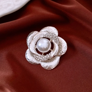 Detail of silver flower brooch with large pearl and brushed metal texture on red silk
