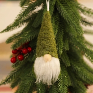 Close-up of a green knitted Christmas gnome hanging on a pine tree with red berries