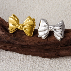 Close-up of gold and silver bow stud earrings on a natural dark wood textured surface