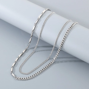 Detail of layered silver metal necklaces featuring Cuban links and flat chain on blue prop