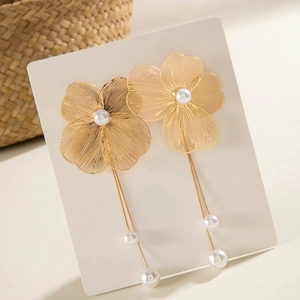 Détail de boucles d'oreilles fleur dorée avec pompons fins et perles blanches