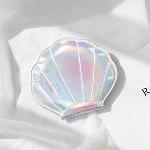 Holographic seashell-shaped portable mirror with iridescent shine on white silk fabric