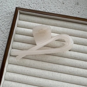 Close-up of translucent beige twisted hair claw clip on a minimalist jewelry display mat