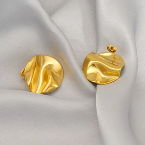 Détail de boucles d'oreilles dorées froissées sur soie montrant une texture métallique