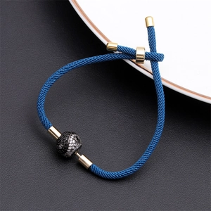 Macro detail of adjustable blue woven rope bracelet with gold metal slider and yin yang bead
