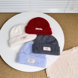 Detail view of four candy-colored double-layer knit beanies with embroidered cloth labels