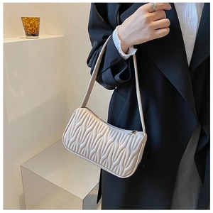 Minimalist beige quilted baguette shoulder bag styled with a professional black trench coat
