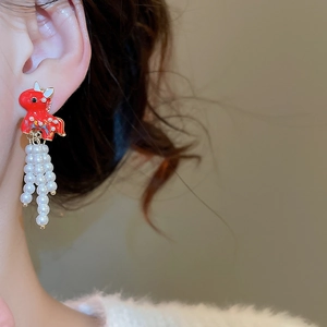 Detail of red enamel dragon earrings with white pearl tassels on model ear