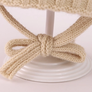 Detail of a creamy beige cable-knit winter hat showing soft bow tie ear straps macro