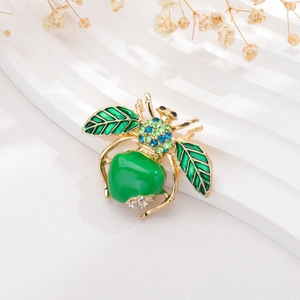 Detailed view of a golden bee brooch with green enamel and sparkling rhinestones