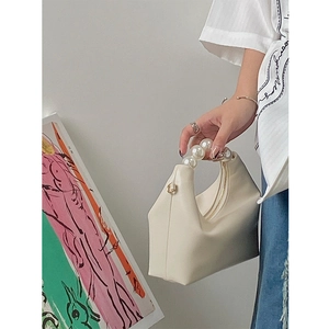 Detail of white PU leather pillow bag featuring a large pearl beaded handle and zipper