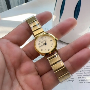 Detailed shot of gold women's watch with cream dial, calendar window and metal strap