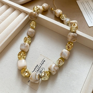 Detail of beaded necklace with beige marble beads and gold plated accents in a jewelry box