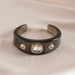 Macro shot of grey resin cuff bracelet with gold-framed crystal on silk fabric
