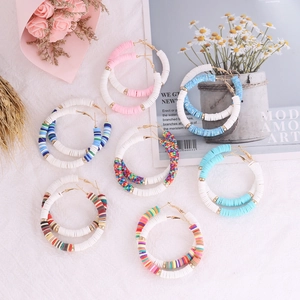 Flat lay of colorful Bohemian Heishi clay bead hoop earrings on artistic white texture