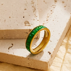 Macro shot of gold eternity ring with square emerald green stones on stone background