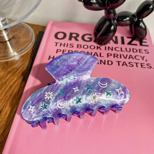 Close-up of acetic hair claw with marbled purple texture and rhinestone stars and moon
