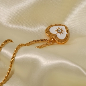 Makroansicht einer goldenen Herz-Halskette mit weißem Emaille und Zirkon auf Seide