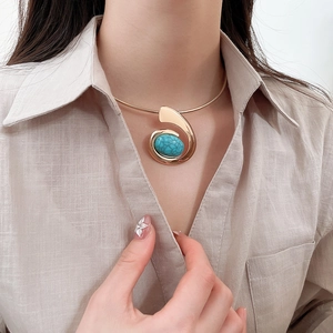 Detail of gold collar necklace with blue turquoise pendant on model in beige shirt