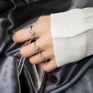 Close-up of classic six-prong silver rings with sparkling round solitaire stones on fingers