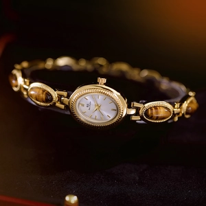 Macro shot of gold vintage watch featuring tiger eye stone links on dark textured surface