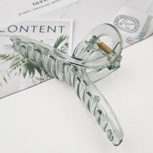 Detail of large translucent sage green hair claw clip with golden spring on marble