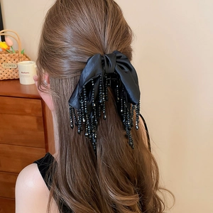 Détail d'une pince à cheveux à nœud en satin noir avec des pompons perlés élégants