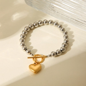 Detail of silver beaded bracelet featuring a gold heart pendant and toggle clasp closure