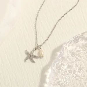 Detail of silver starfish pendant necklace with zircons and white pearl on white stone