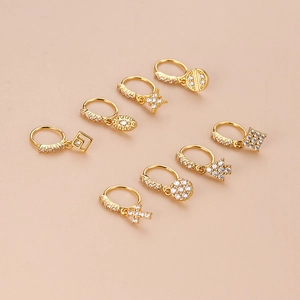 Set of 8 golden geometric nose rings and earrings with zircon accents on pink background