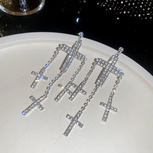 Elegant silver cross tassel earrings with sparkling crystals on white ceramic plate