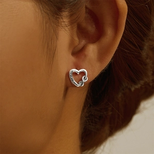 Macro detail of silver hollow heart stud earrings with engraved letters and knot texture