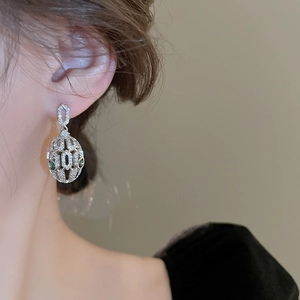Detail view of silver oval hoop earring with pavé crystals and green gemstone on model