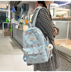 Detail of light blue backpack with strawberry patterns and a white plush keychain accessory