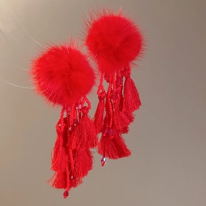 Detailed shot of red pompom earrings with beaded strands and layered silk tassels