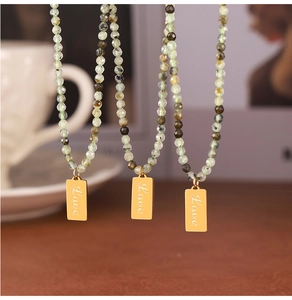 Detailed close-up of golden Love pendants with natural green stone beaded necklaces