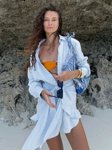 Detail of light blue button-down shirt dress with waist tie knot in a beach resort setting