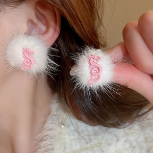 Close-up of white plush pom-pom earring with a pink dragon motif shown on a model