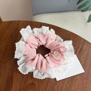 Detail von rosa-weiß kariertem Haargummi mit Spitzenborte und Schleife auf Holztisch