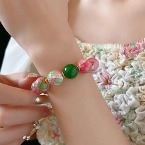 Detail of pink and green floral ceramic beads on gold plated bracelet worn by a model