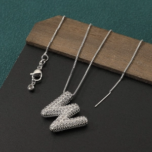 Close-up of silver pave-set letter W pendant necklace with cubic zirconia on wooden surface
