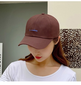 Detailed embroidery of a blue whale on a dark brown cotton baseball cap worn by model