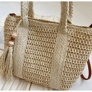 Detail of beige straw tote bag with intricate hollow weave, wood beads and tassel