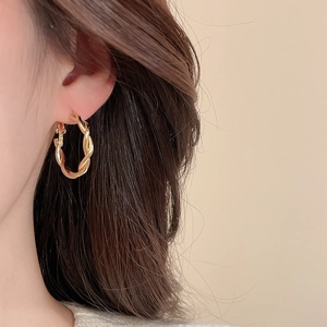 Close-up of elegant gold twisted hoop earrings with textured spiral design on a model