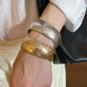 Détails des motifs floraux embossés sur les bracelets larges en métal doré et argenté
