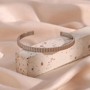 Close-up of a silver stainless steel open bangle with vertical grooved texture on silk