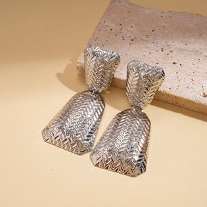 Macro shot of silver textured geometric earrings on stone backdrop with metallic details