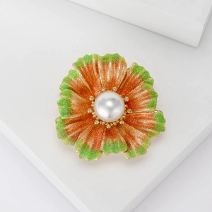 Detail of flower brooch with orange and green petals, gold glitter, and a large white pearl