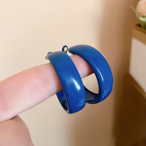 Macro view of minimalist deep blue hoop earrings held to show texture and large size